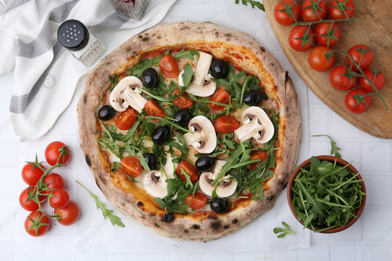 Photo of Tasty pizza with cherry tomatoes, black olives, mushrooms and arugula on white tiled table, flat lay