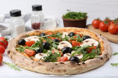 Photo of Tasty pizza with cherry tomatoes, black olives, mushrooms and arugula on white table, closeup