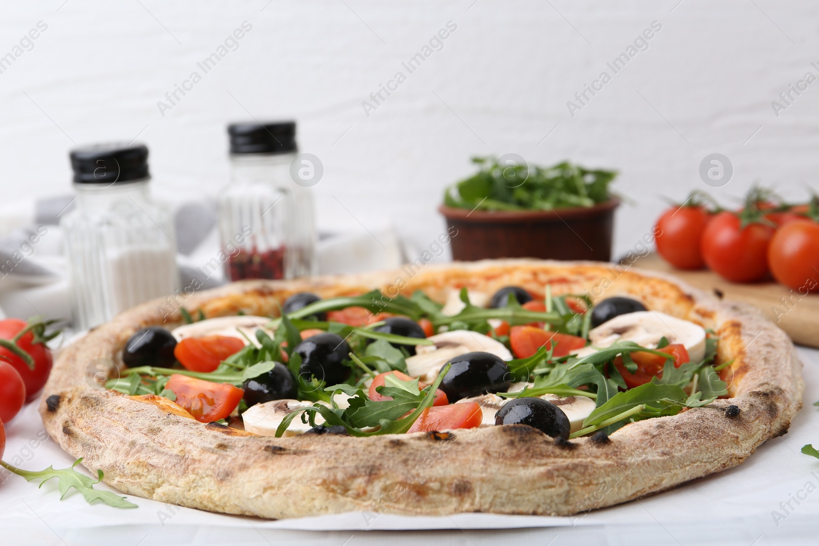 Photo of Tasty pizza with cherry tomatoes, black olives, mushrooms and arugula on white table, closeup