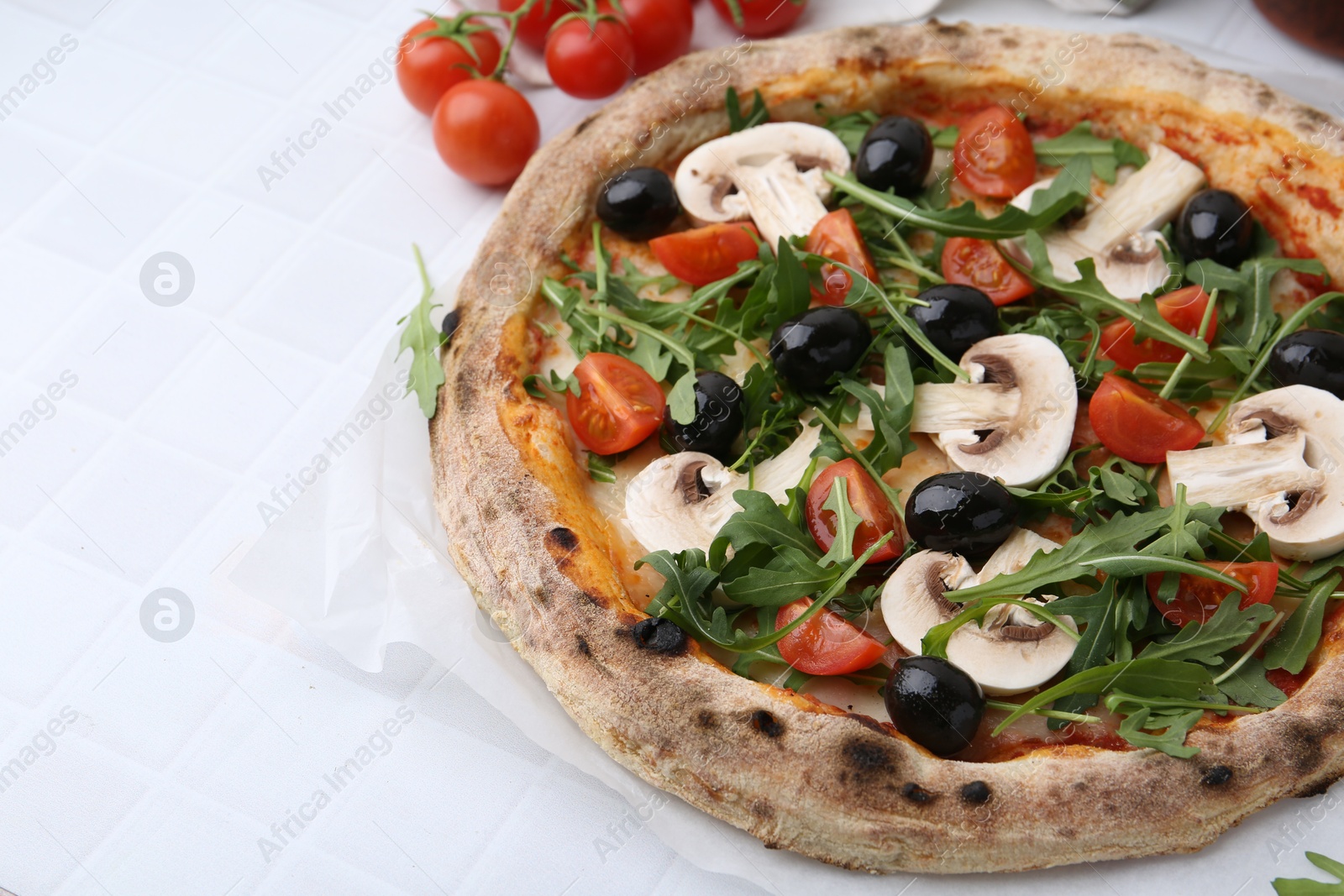 Photo of Tasty pizza with cherry tomatoes, black olives, mushrooms and arugula on white tiled table, closeup. Space for text