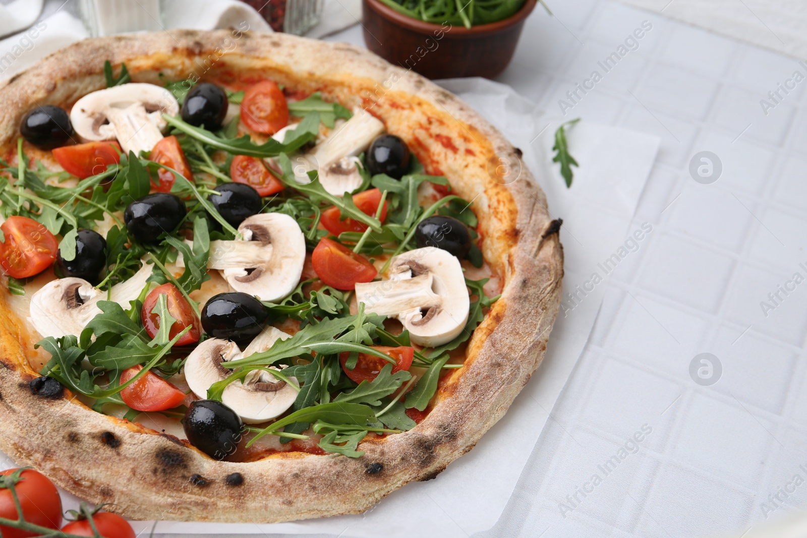 Photo of Tasty pizza with cherry tomatoes, black olives, mushrooms and arugula on white tiled table, closeup. Space for text