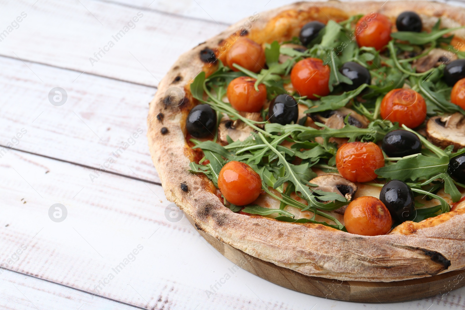 Photo of Tasty pizza with cherry tomatoes, black olives, mushrooms and arugula on white wooden table, closeup. Space for text