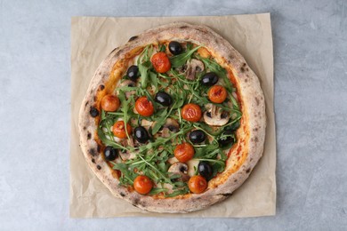 Photo of Tasty pizza with cherry tomatoes, black olives, mushrooms and arugula on grey table, top view