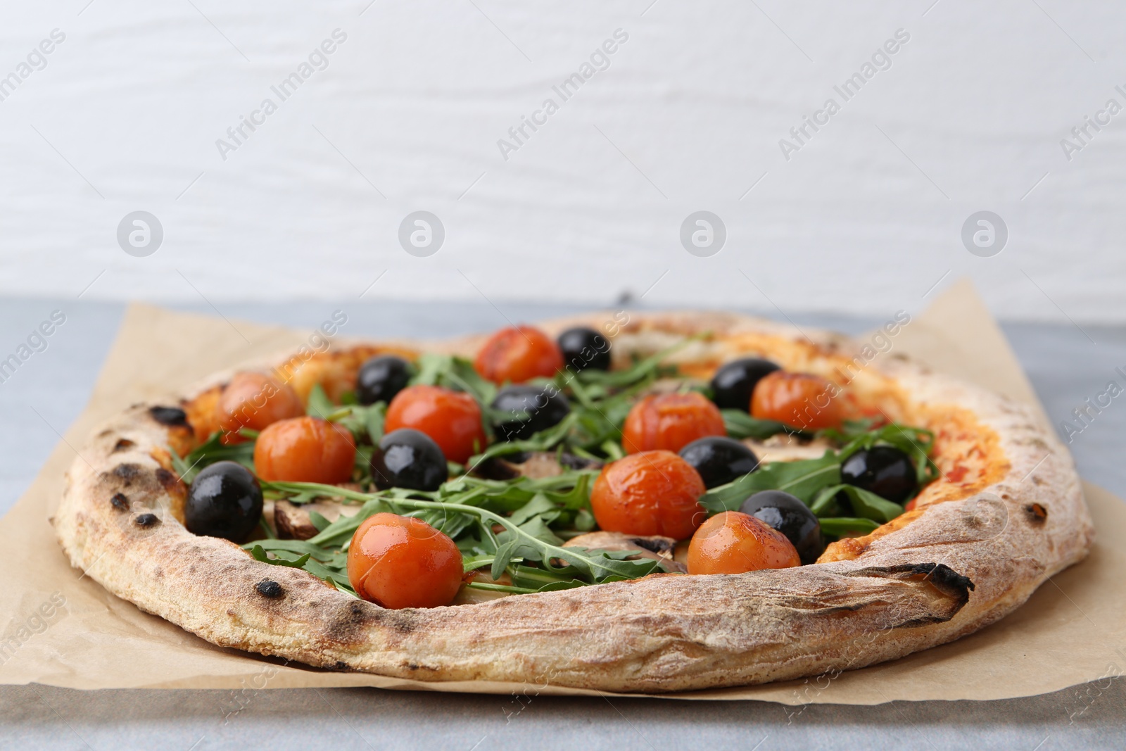 Photo of Tasty pizza with cherry tomatoes, black olives, mushrooms and arugula on grey table, closeup