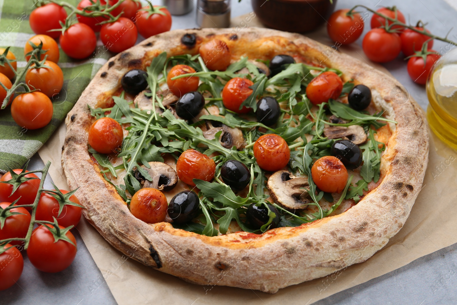 Photo of Tasty pizza with cherry tomatoes, black olives, mushrooms and arugula on grey table, closeup