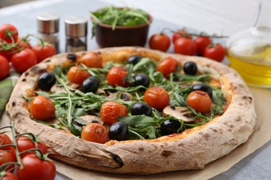 Photo of Tasty pizza with cherry tomatoes, black olives, mushrooms and arugula on grey table, closeup