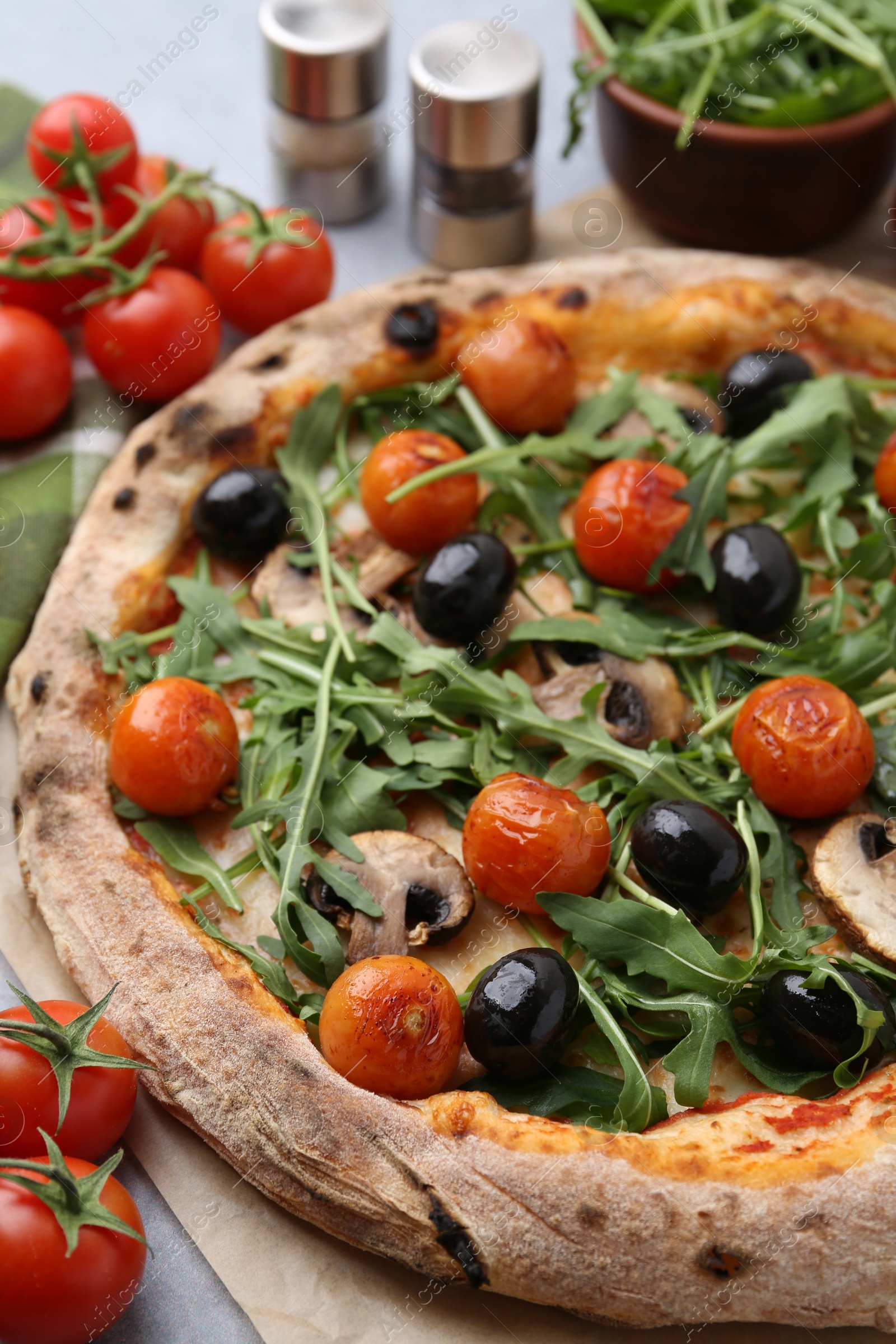 Photo of Tasty pizza with cherry tomatoes, black olives, mushrooms and arugula on grey table, closeup