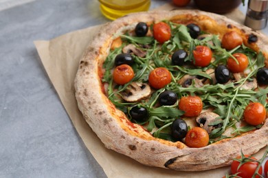 Photo of Tasty pizza with cherry tomatoes, black olives, mushrooms and arugula on grey table, closeup