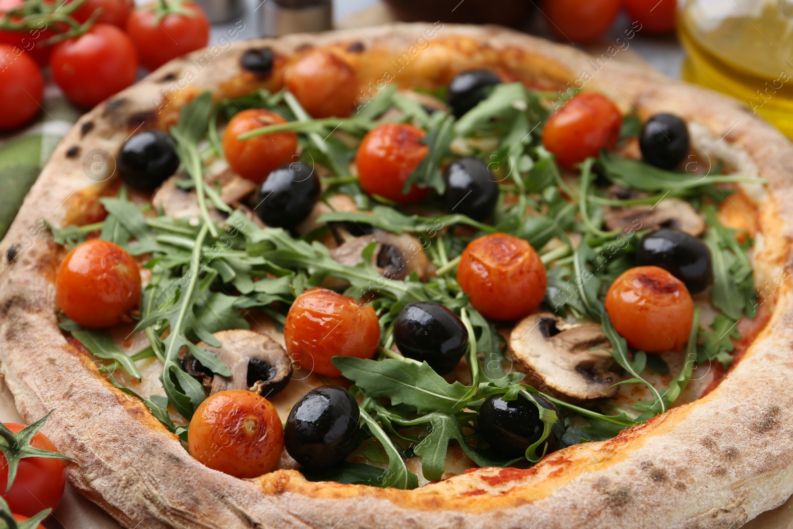 Photo of Tasty pizza with cherry tomatoes, black olives, mushrooms and arugula on table, closeup