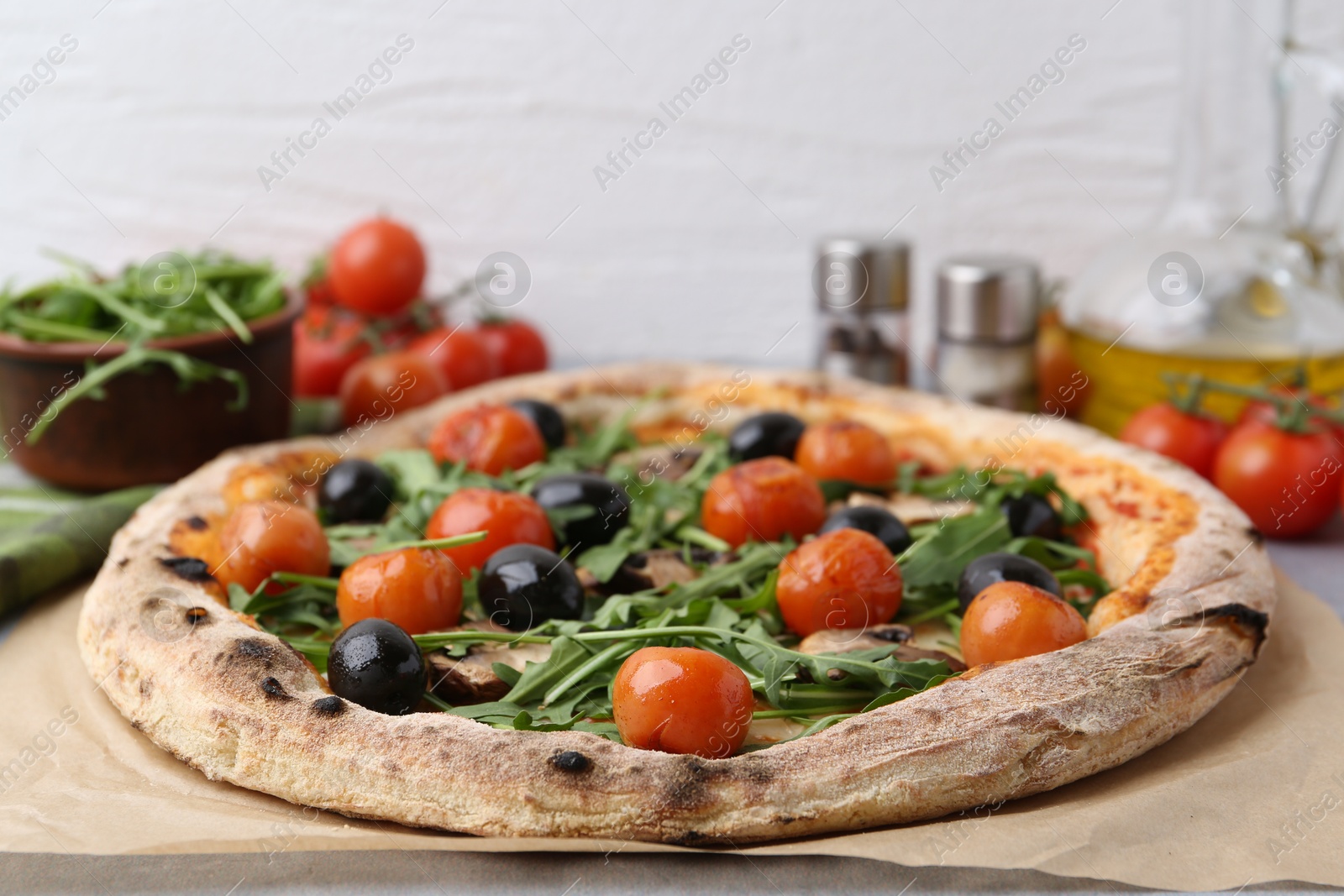 Photo of Tasty pizza with cherry tomatoes, black olives, mushrooms and arugula on table, closeup