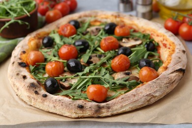 Photo of Tasty pizza with cherry tomatoes, black olives, mushrooms and arugula on table, closeup