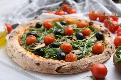 Photo of Tasty pizza with cherry tomatoes, black olives, mushrooms and arugula on white table, closeup