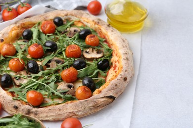 Photo of Tasty pizza with cherry tomatoes, black olives, mushrooms and arugula on white table, closeup. Space for text