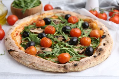 Photo of Tasty pizza with cherry tomatoes, black olives, mushrooms and arugula on white table, closeup