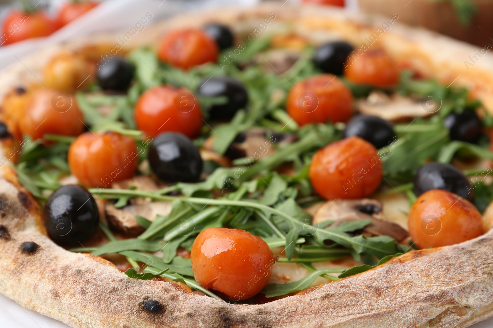 Photo of Tasty pizza with cherry tomatoes, black olives, mushrooms and arugula on table, closeup