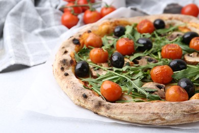 Photo of Tasty pizza with cherry tomatoes, black olives, mushrooms and arugula on white table, closeup. Space for text