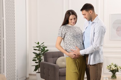 Photo of Man trying to feel baby kicks in his pregnant wife's belly at home. Space for text