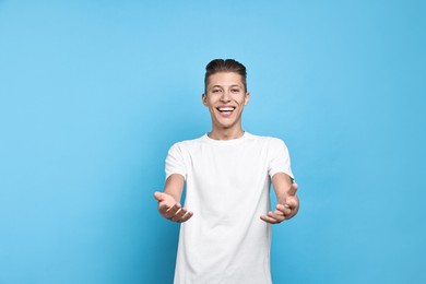 Photo of Happy man welcoming friends or guests on light blue background