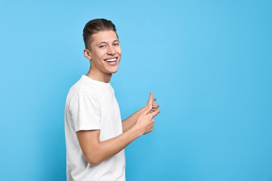 Photo of Happy man welcoming friends or guests on light blue background. Space for text