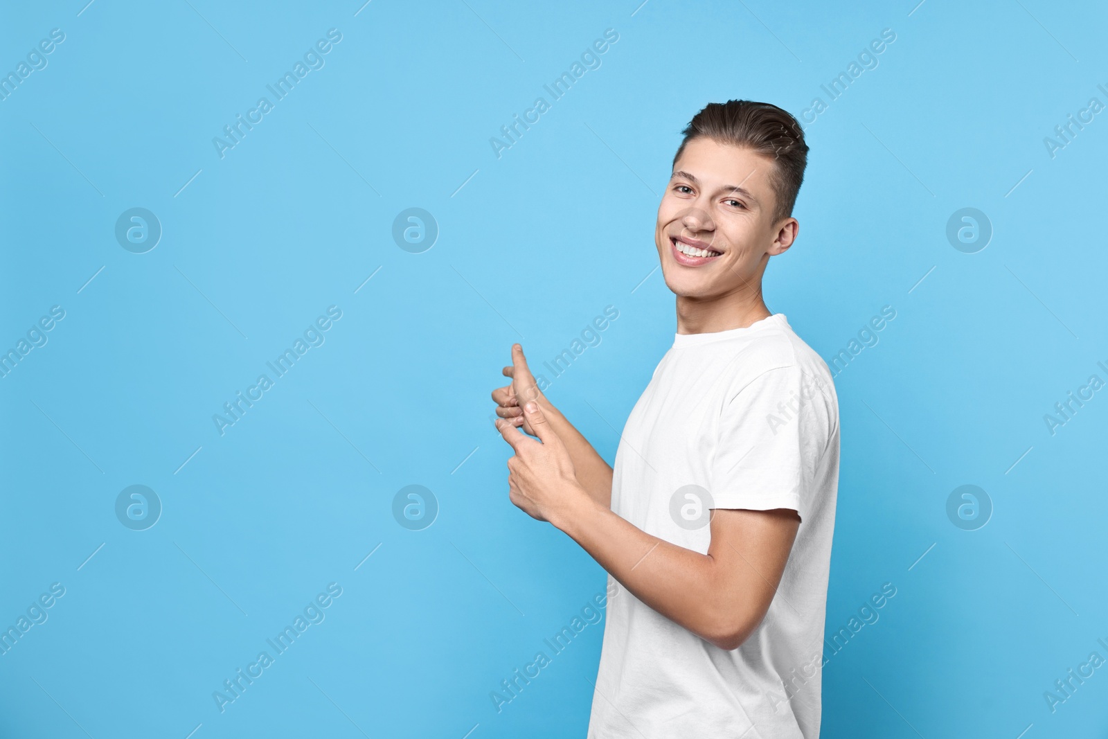 Photo of Happy man welcoming friends or guests on light blue background. Space for text