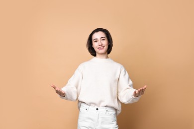 Photo of Cheerful woman welcoming friends or guests on brown background