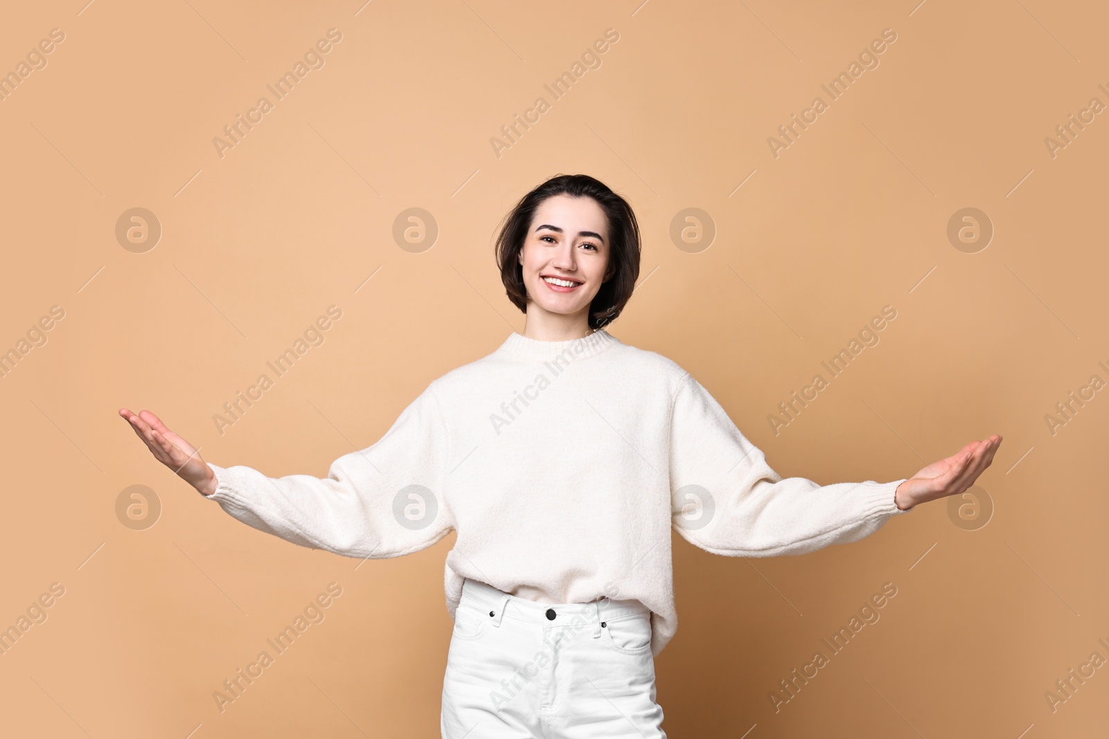 Photo of Cheerful woman welcoming friends or guests on brown background