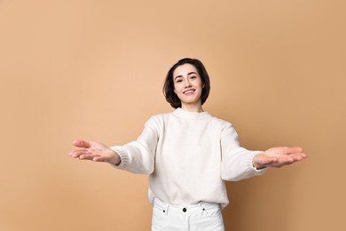 Photo of Cheerful woman welcoming friends or guests on brown background