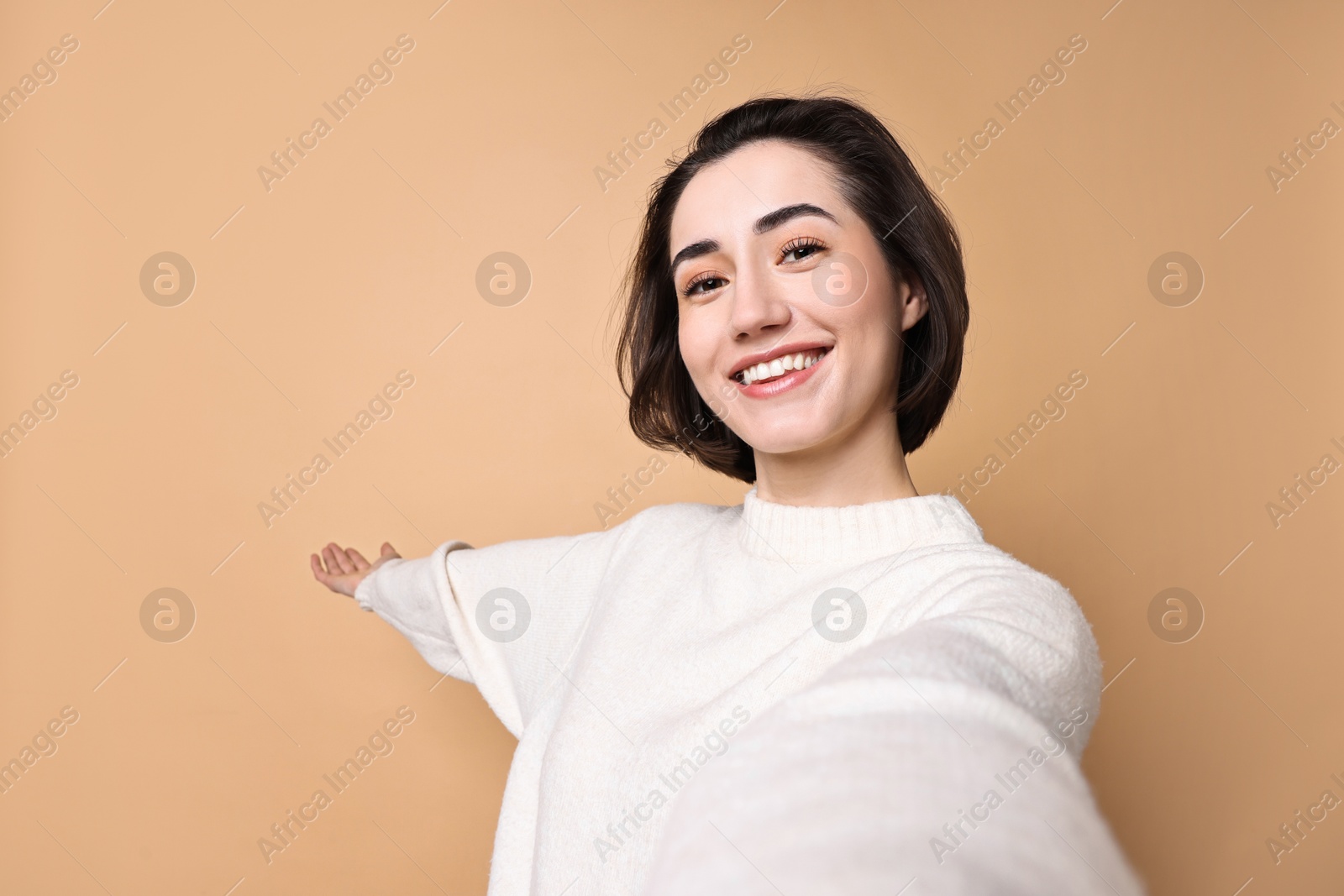 Photo of Cheerful woman welcoming friends or guests via video call on brown background