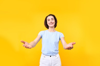 Photo of Cheerful woman welcoming friends or guests on yellow background