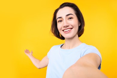 Photo of Cheerful woman welcoming friends or guests via video call on yellow background