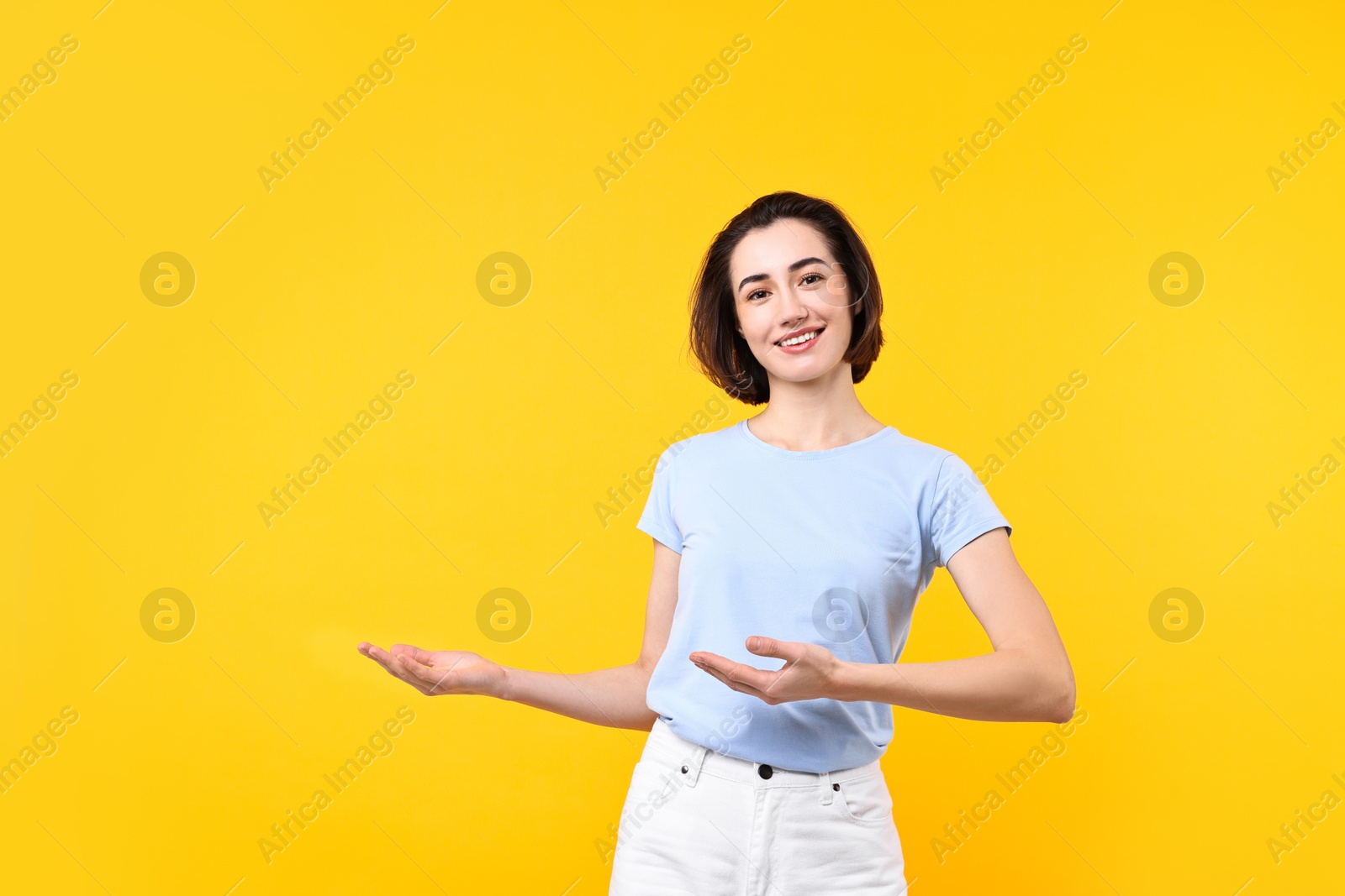 Photo of Cheerful woman welcoming friends or guests on yellow background