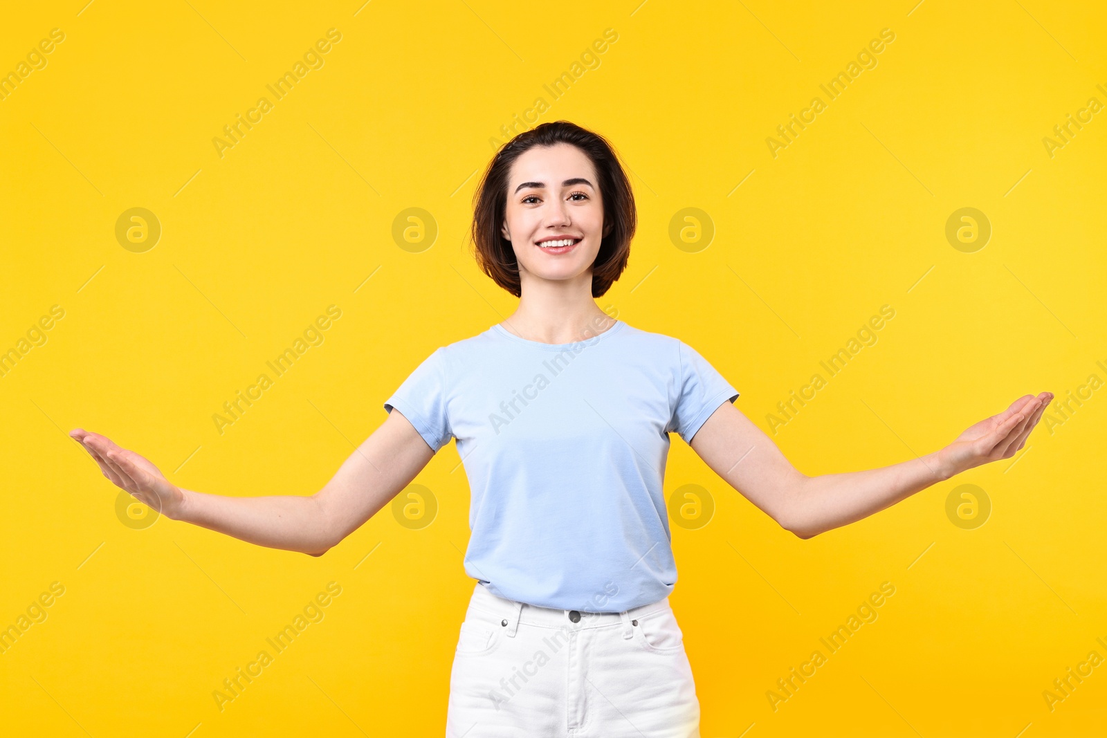 Photo of Cheerful woman welcoming friends or guests on yellow background