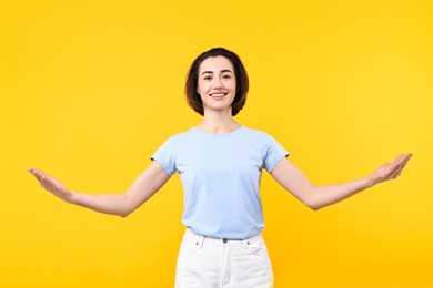 Photo of Cheerful woman welcoming friends or guests on yellow background