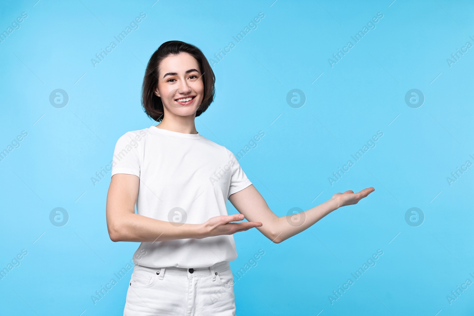 Photo of Cheerful woman welcoming friends or guests on light blue background