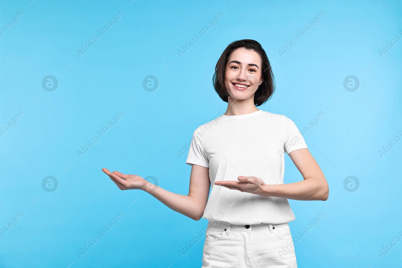 Photo of Cheerful woman welcoming friends or guests on light blue background