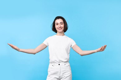 Photo of Cheerful woman welcoming friends or guests on light blue background