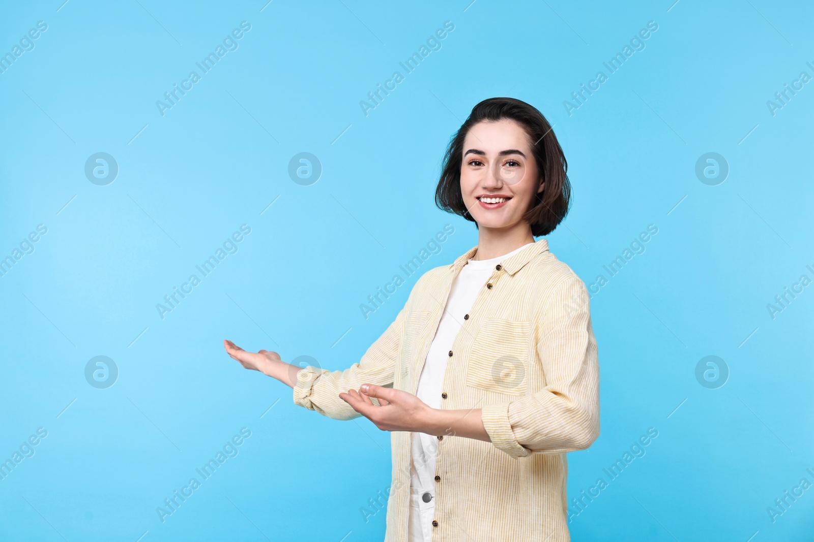 Photo of Cheerful woman welcoming friends or guests on light blue background