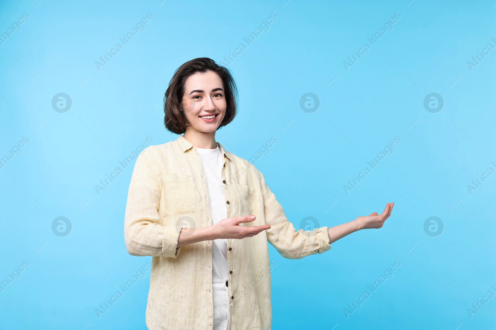 Photo of Cheerful woman welcoming friends or guests on light blue background