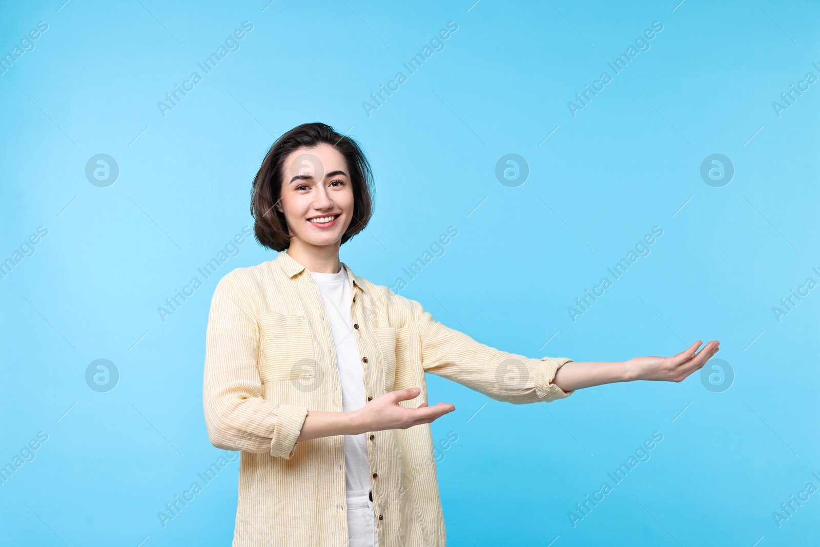 Photo of Cheerful woman welcoming friends or guests on light blue background