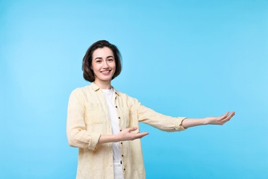 Photo of Cheerful woman welcoming friends or guests on light blue background