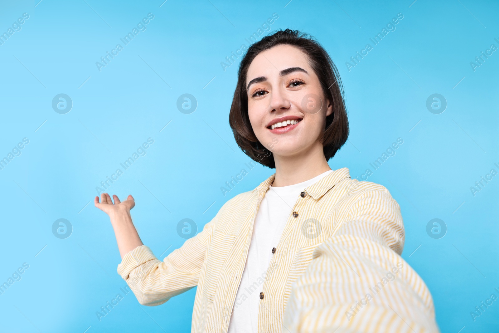 Photo of Cheerful woman welcoming friends or guests via video call on light blue background