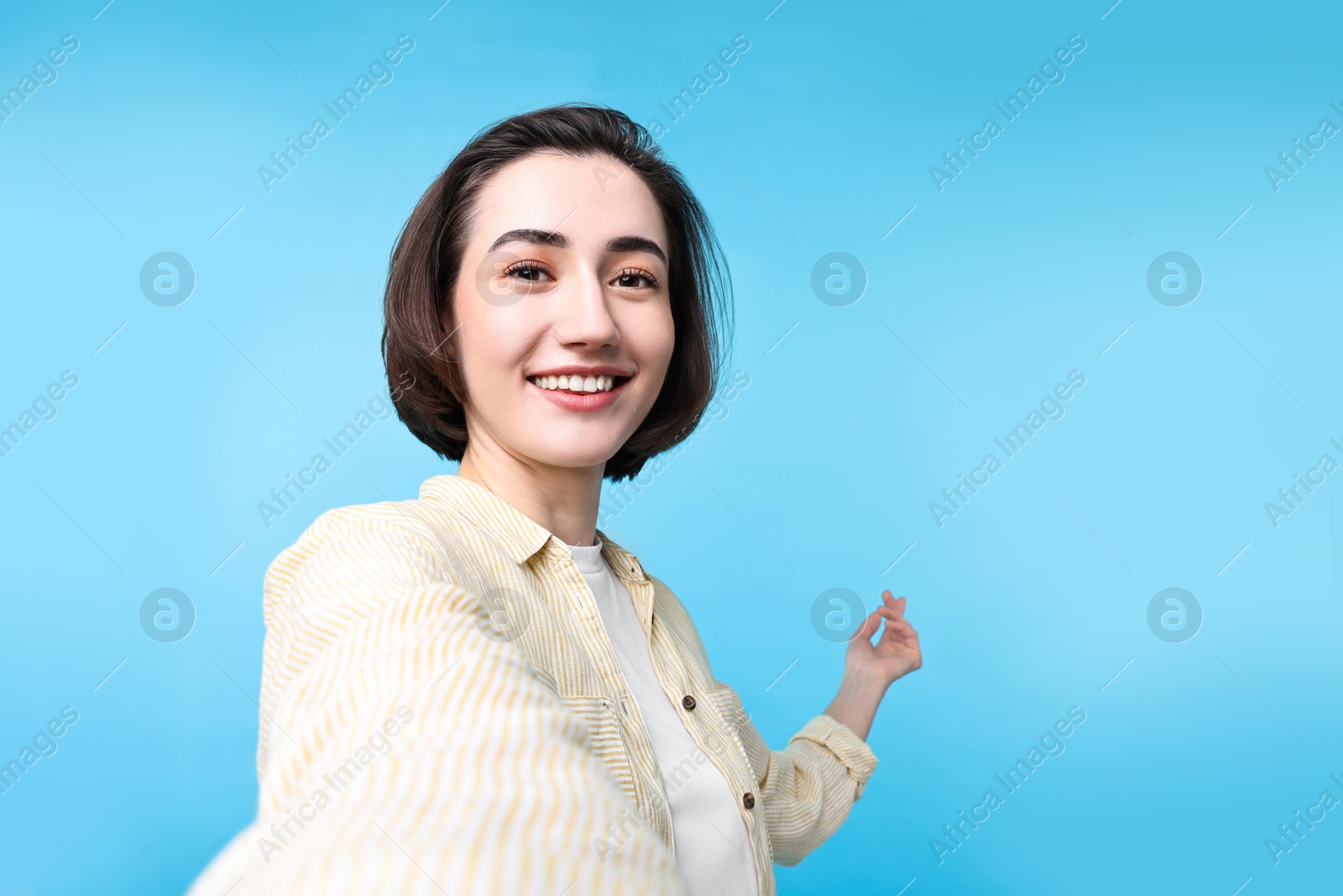 Photo of Cheerful woman welcoming friends or guests via video call on light blue background