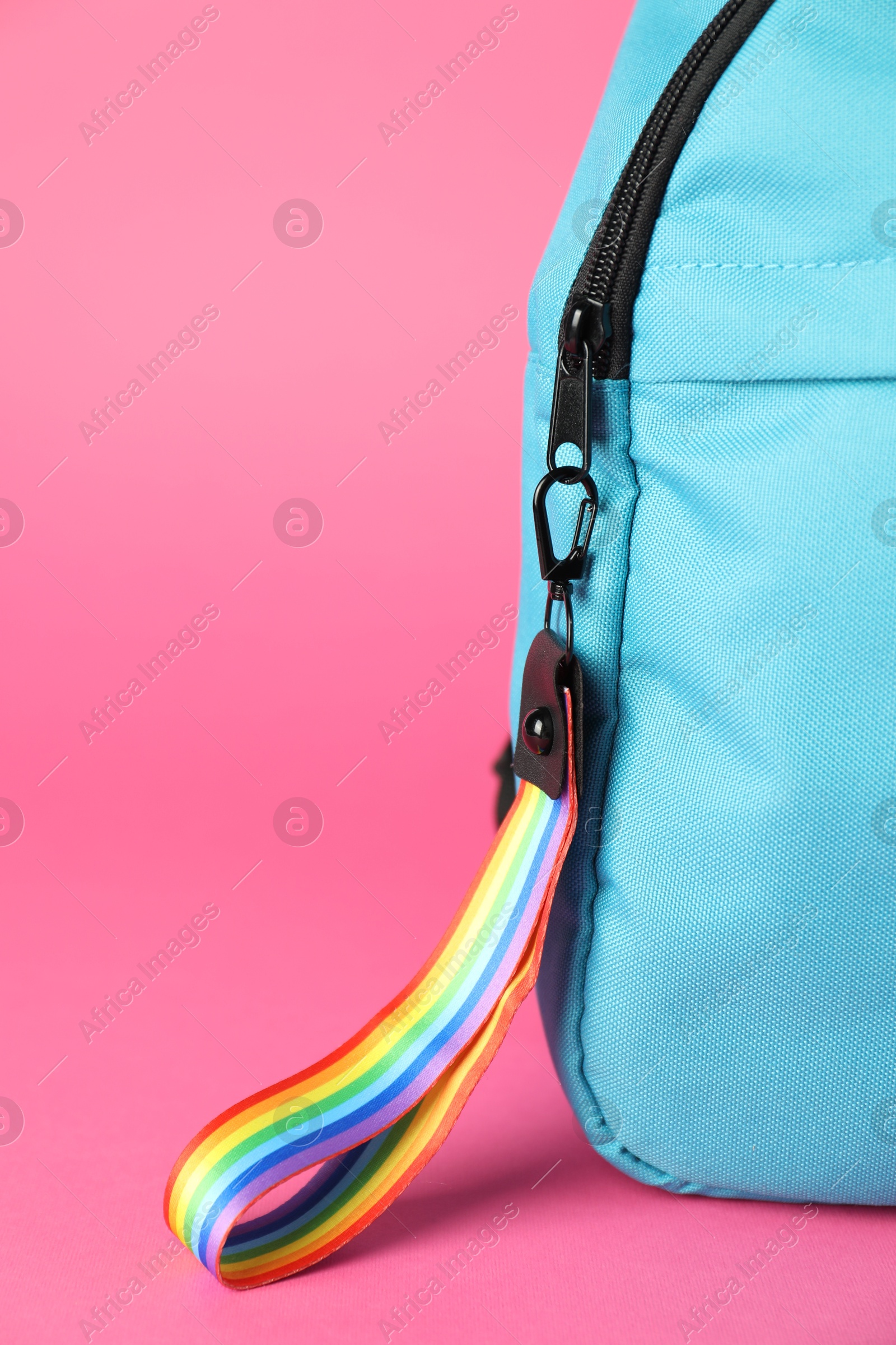 Photo of Backpack with keychain in LGBT colors on pink background, closeup. Space for text