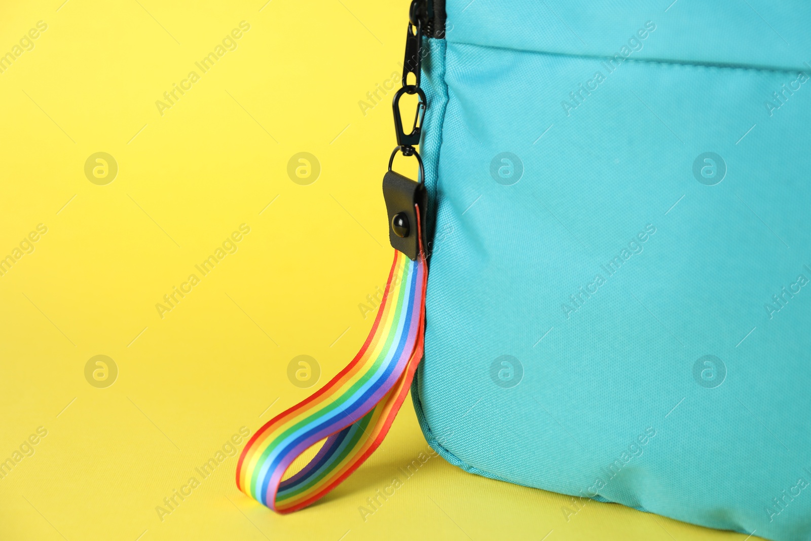 Photo of Backpack with keychain in LGBT colors on yellow background, closeup. Space for text