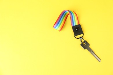 Photo of Key with keychain in LGBT colors on yellow background, top view. Space for text