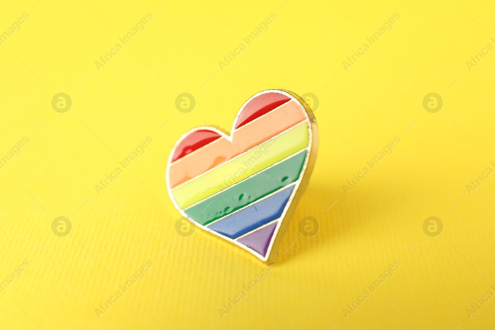 Photo of Heart shaped badge in LGBT colors on yellow background, closeup