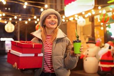 Photo of Happy woman with Christmas gifts and paper cup at fair