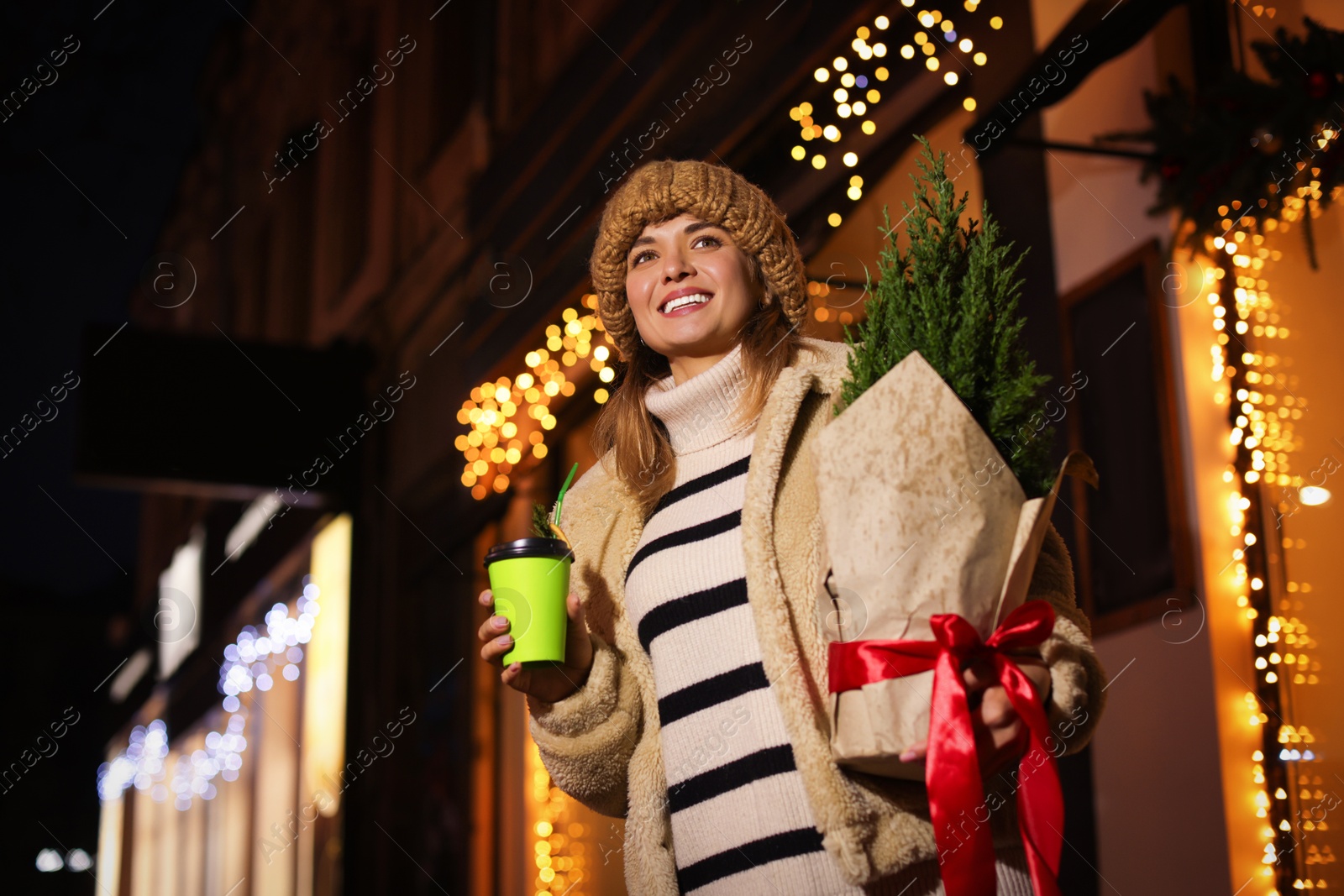 Photo of Happy woman with thuja tree and paper cup outdoors, low angle view. Space for text