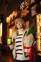 Photo of Happy woman with thuja tree and paper cup outdoors