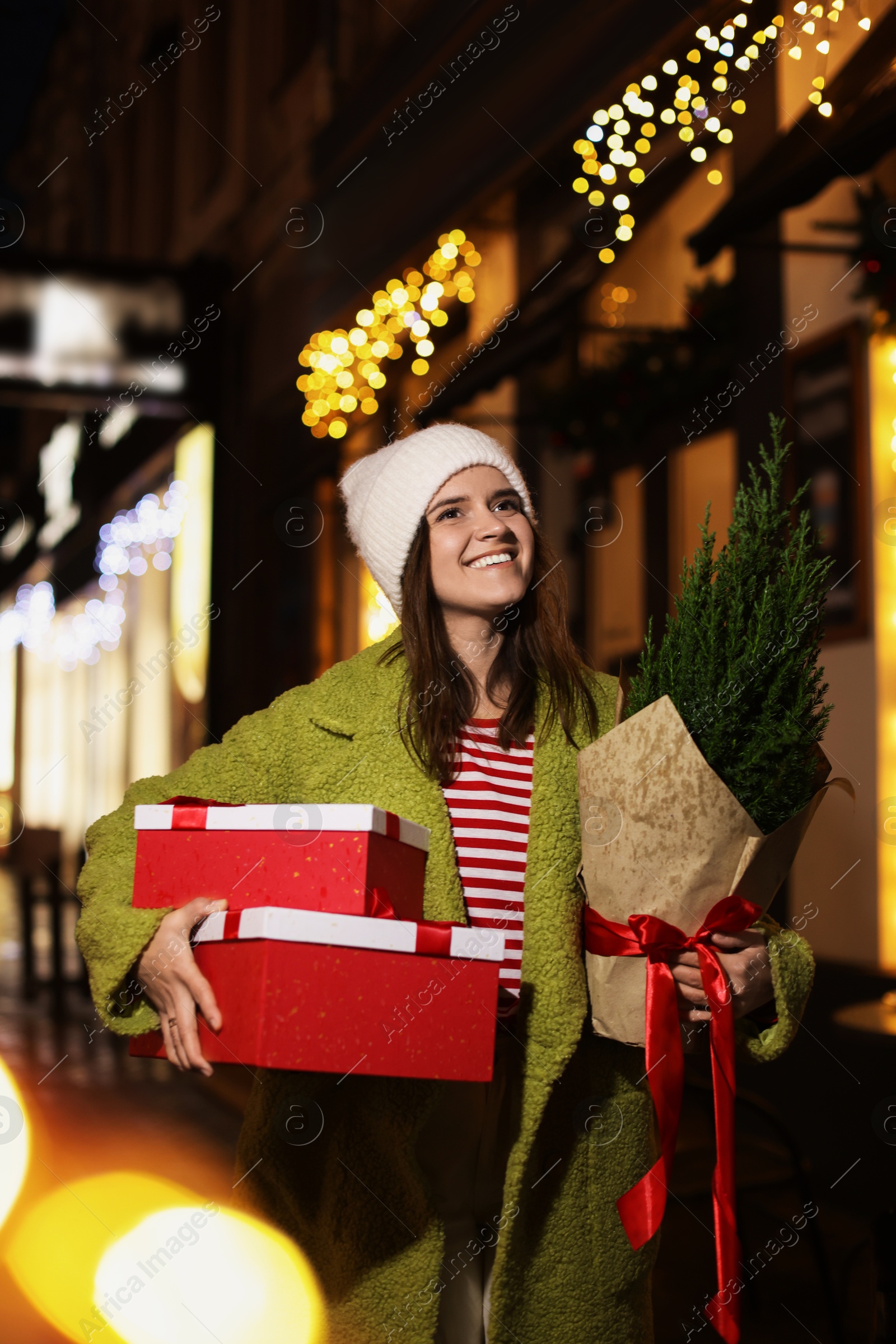 Photo of Happy woman with thuja tree and Christmas gifts outdoors, bokeh effect